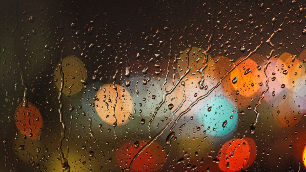 Close-up of raindrops on glass with blurred colorful city lights in the background.